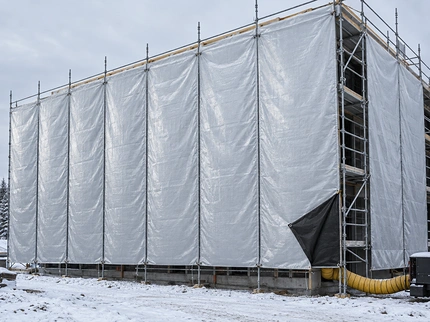 Building scaffolding enclosed with silver insulated construction tarps in winter, one corner folded back to show the black underside